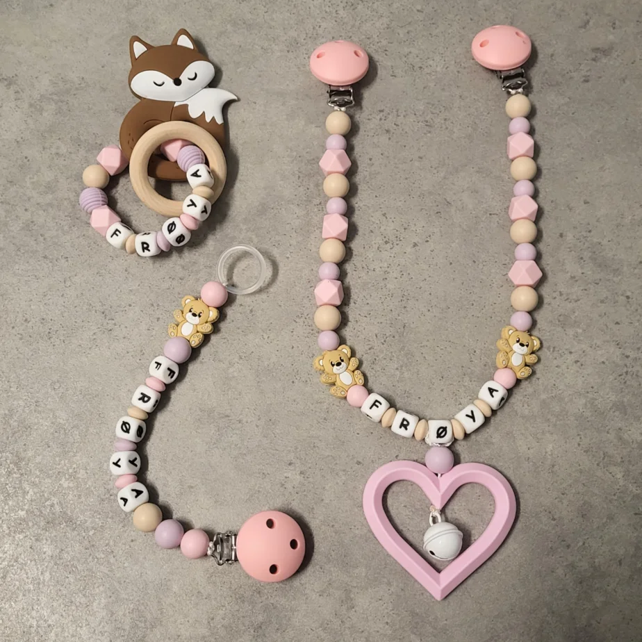Personlig gavesett til baby med vognlenke, bitering og smokkelenke i babyrosa, beige og duse farger.